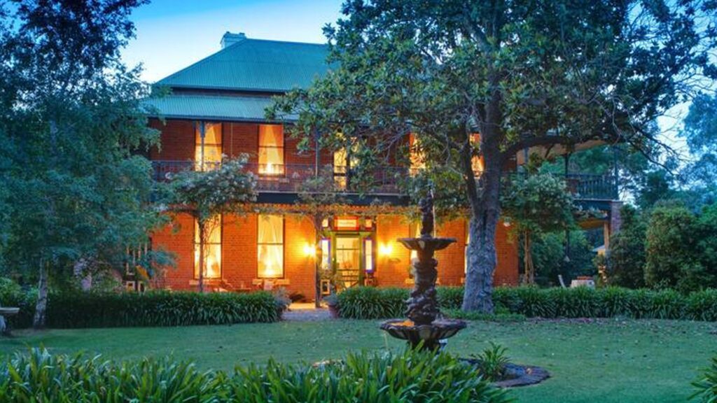 The charming country-style facade of Koendidda Country Retreat in the gardens with a water fountain, one of country Victoria's best luxury accommodation - Luxury Escapes