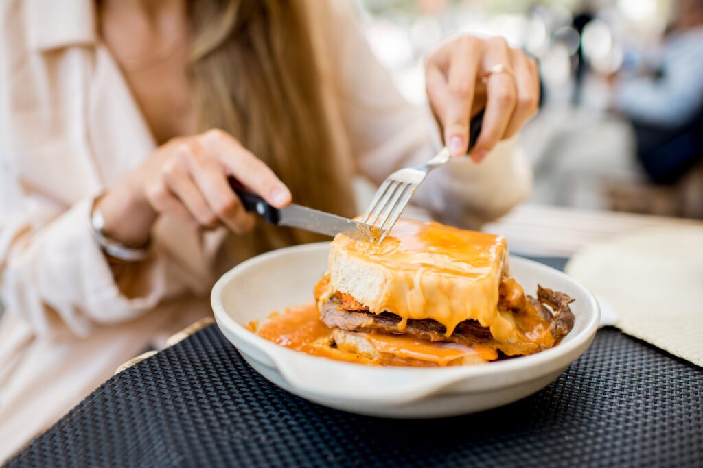 A woman eating a Portuguese sandwich called a Francesinha - Luxury Escapes 