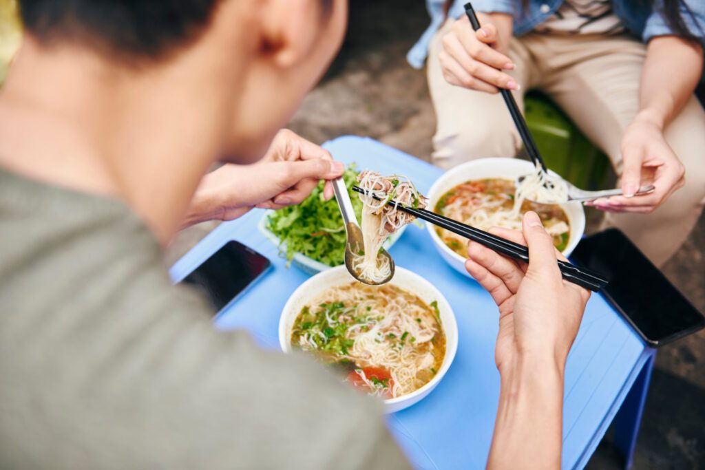 Two people digging into the popular fragrant dish of Hanoi - Pho - Luxury Escapes