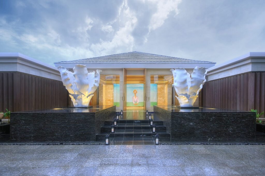 The grand entrance way to The Mulia Spa at the Mulia Bali resort, featuring two large flower sculptures atop two water features - Luxury Escapes