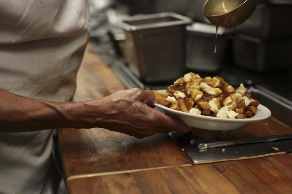 A chef pours gravy onto a bowl of poutine, one of the many things to experience in Canada during the winter - Luxury Escapes