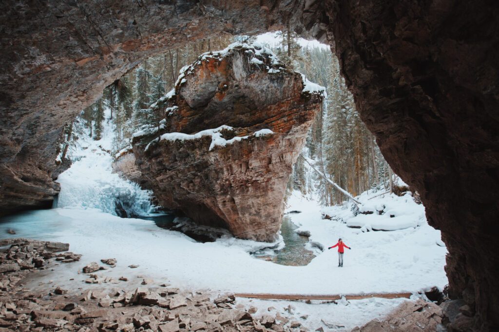 A person in snow gear walking under the Johnston Canyon, one of the many things to experience in Canada during the winter - Luxury Escapes