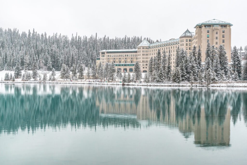 The snow covered  facade of Fairmont Château Lake Louise overlooking a lake, one of the many things to experience in Canada during the winter - Luxury Escapes