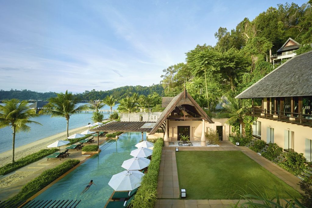 Tropischer Resort-Pool neben einer bewaldeten Bucht.