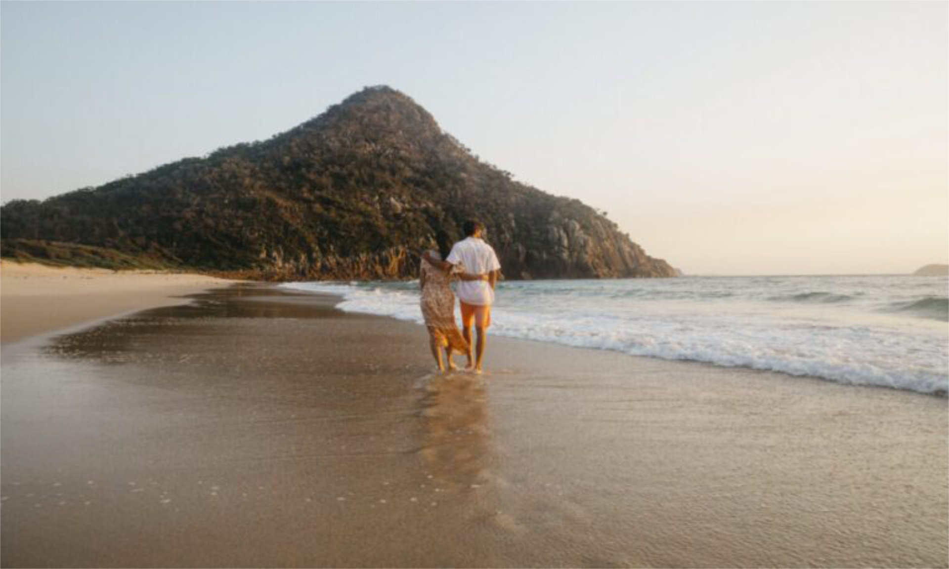 Couple walking on an Australia beach, one of Australia's best babymoon destinations - Luxury Escapes