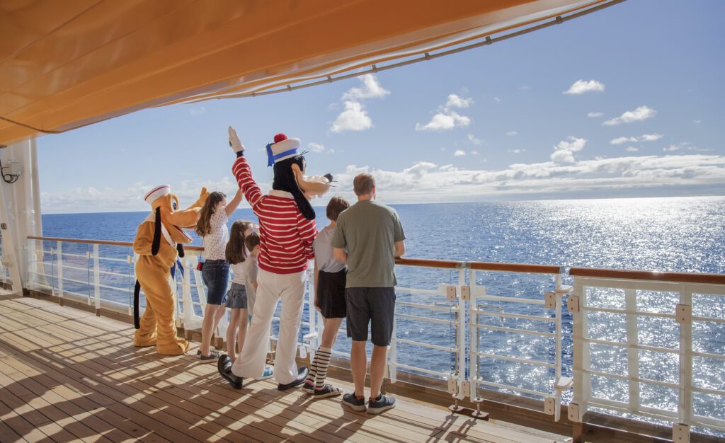 Disney characters and excited guests gaze into the sunset from the deck of the Disney Wonder, to illustrate why you should book with Disney Cruise Line for 2024 - Luxury Escapes