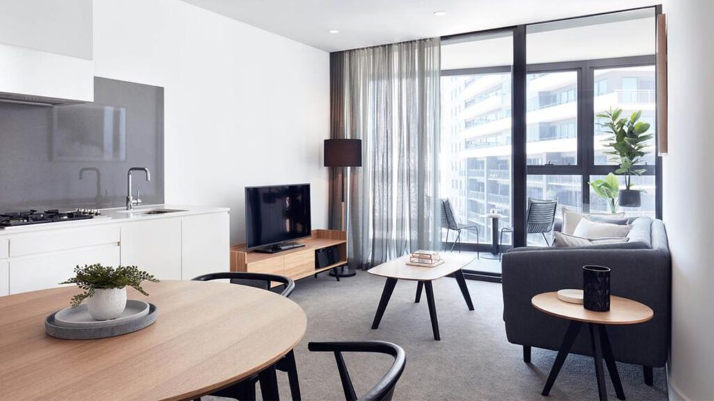 The interiors of a modern apartment within Shadow Play by Peppers with white walls, a grey couch, TV and a balcony in the background - one of the best family friendly resorts in the world - Luxury Escapes
