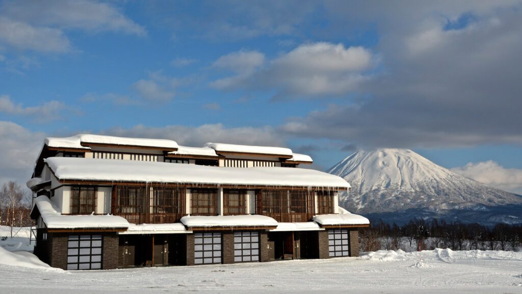 A wooden building covered in snow with a snow capped mountain in the background which make up Kasara Niseko Village Townhouse - one of the best family friendly resorts in the world - Luxury Escapes