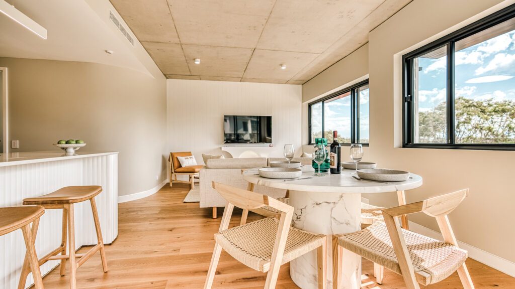 The kitchen area of one of Essence Peregian Beach's self contained apartments with wooden chairs, marble tables and a small lounge area which is part of one of the best family friendly resorts in the world - Luxury Escapes