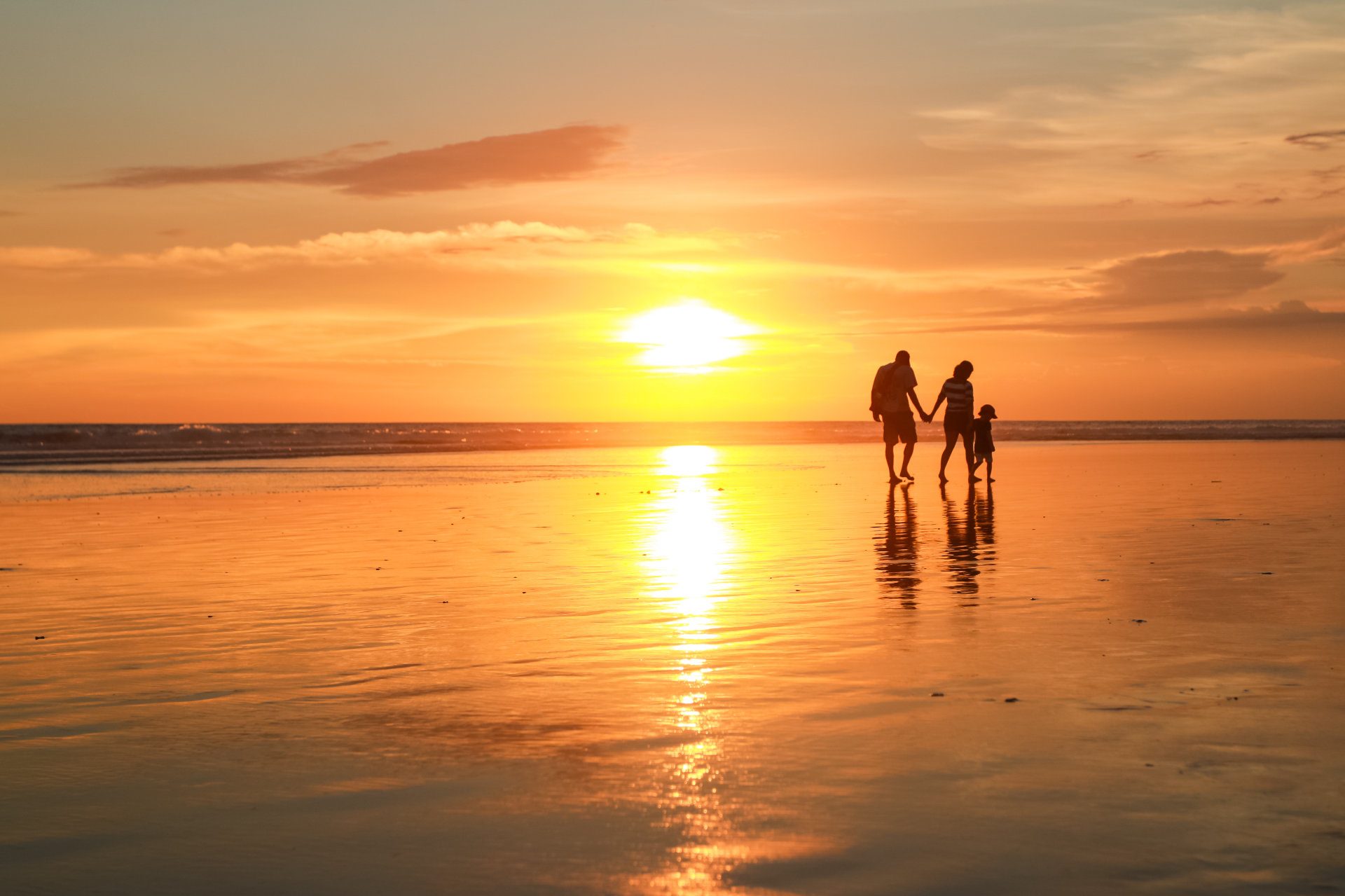 A small family walk along the beach at one of the world's best family resorts - Luxury Escapes