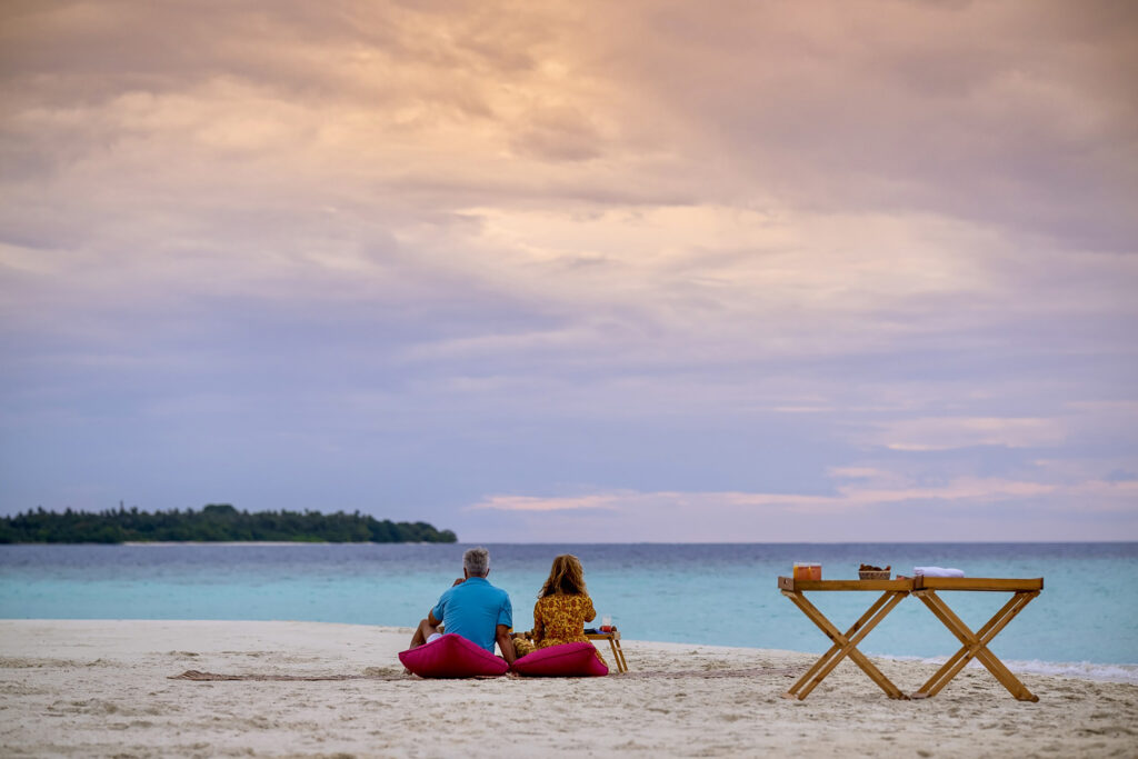 Two people sitting on the beach in the Maldives, having a picnic - Luxury Escapes 