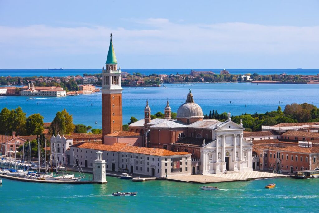 A stunning aerial shot of San Giorgio Maggiore, featured in A Haunting in Venice surrounded by the canals which is one of the best filming locations to visit in the world - Luxury Escapes