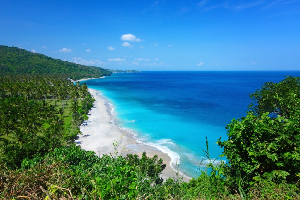 A view of a beach and blue sky in Lombok, one of the best islands to visit in Indonesia - Luxury Escapes