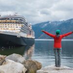 A cruise in Alaska with a girl standing with her arms open, embracing the happy moment - Luxury Escapes