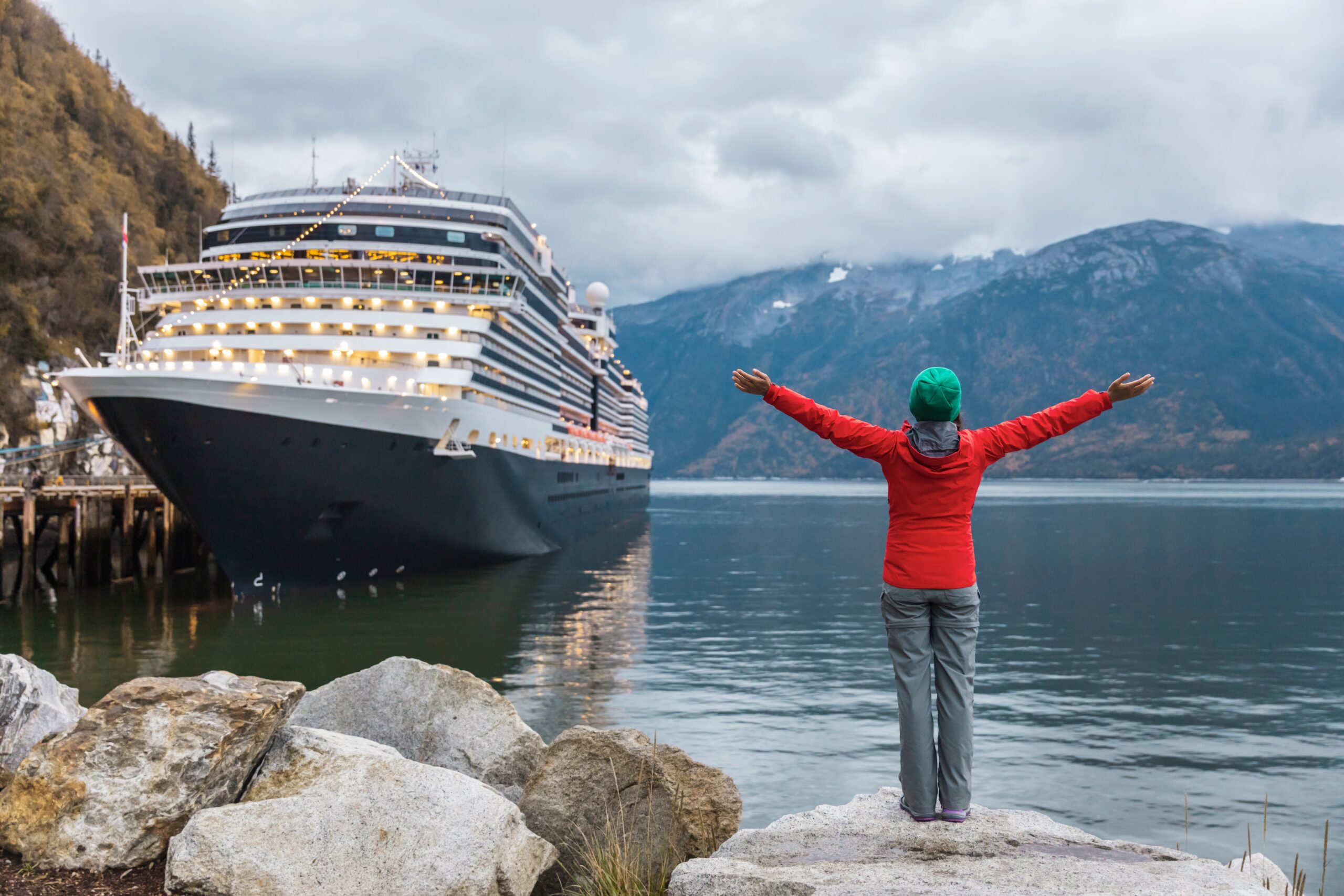 A stunning image of a cruise in Alaska with a girl standing with her arms open, embracing the happy moment - Luxury Escapes