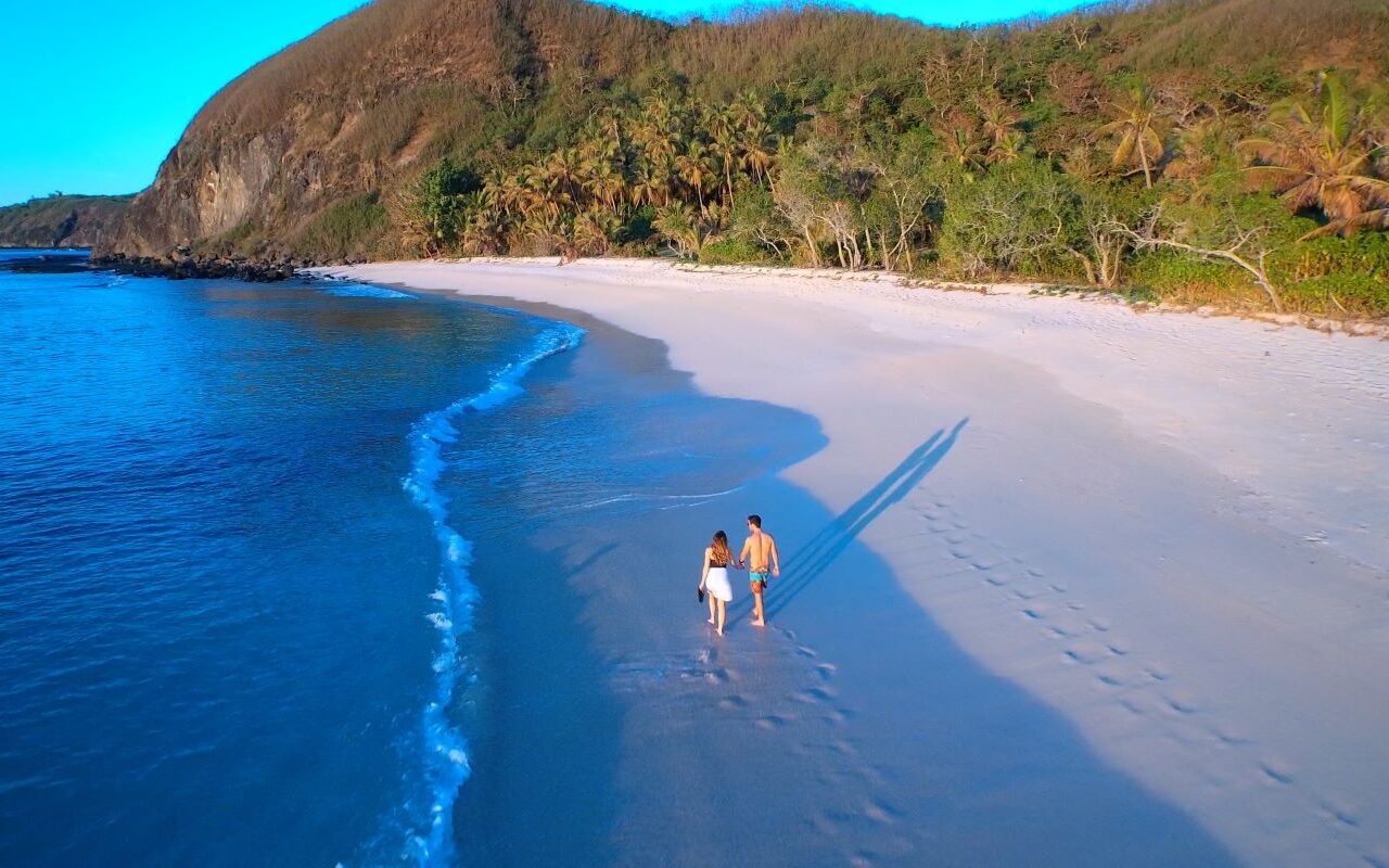 A couple walking on the private beachfront at Yasawa Island Resort & Spa, one of Fiji's best all inclusive resorts - Luxury Escapes