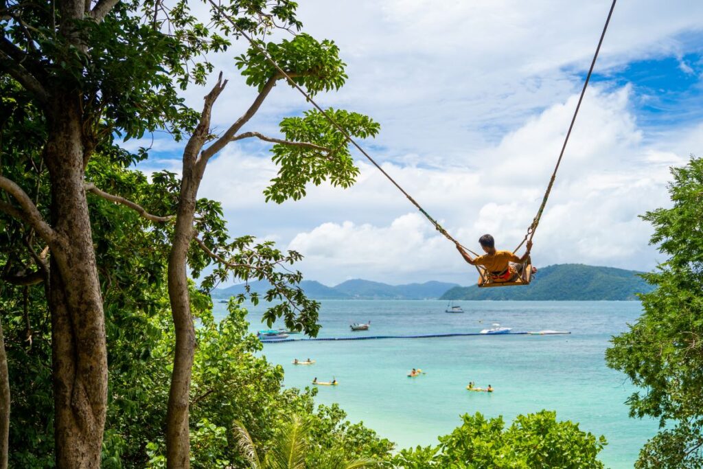 A tourist swinging on a swing in front of Banana Beach - Luxury Escapes