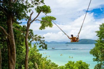 A tourist swinging on a swing in front of Banana Beach