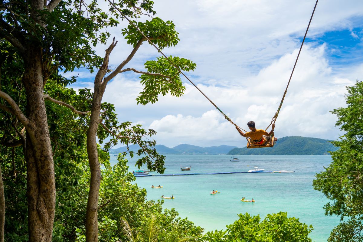 A tourist swinging on a swing in front of Banana Beach