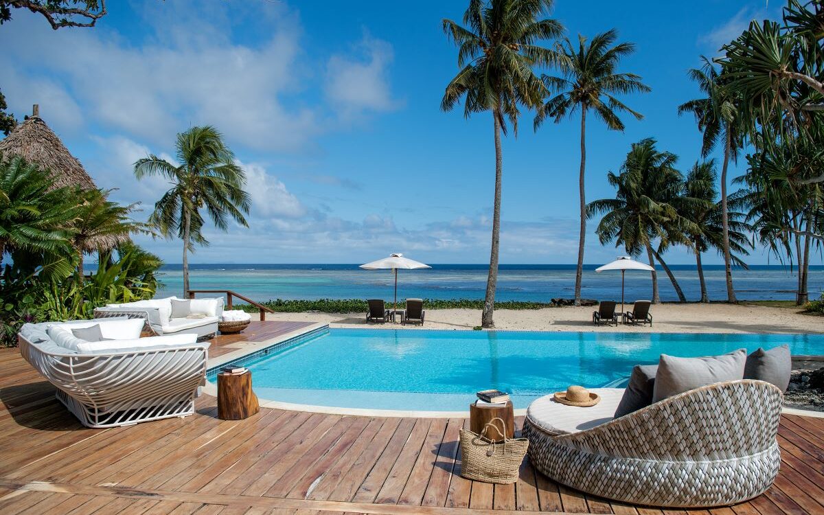 Tranquil pool area fringed by palm trees overlooking the beach at Wakaya Club and Spa, one of Fiji's best all-inclusive resorts - Luxury Escapes