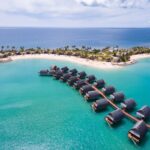 An aerial shot of the blue sea and a row of over water villas at Fiji Marriott Resort Momi Bay which is one of the best long weekend stays from Brisbane to Fiji - Luxury Escapes