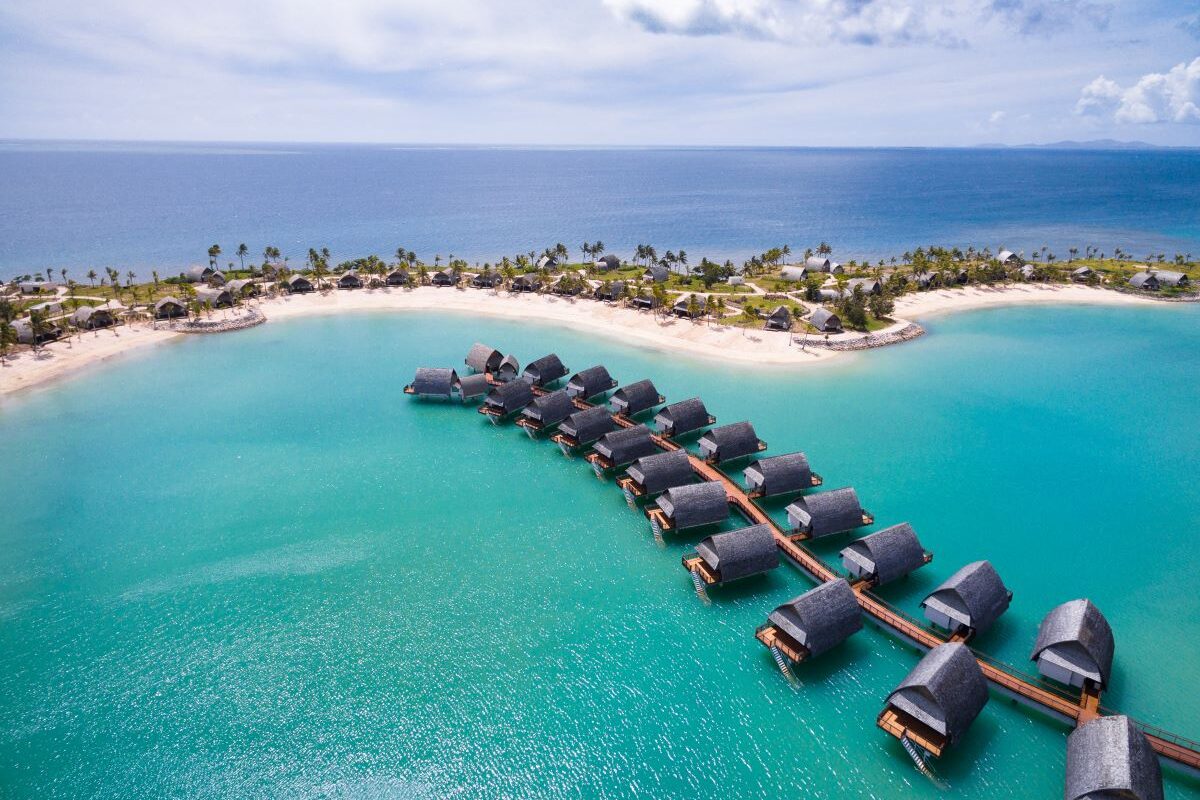 An aerial shot of the blue sea and a row of over water villas at Fiji Marriott Resort Momi Bay which is one of the best long weekend stays from Brisbane to Fiji - Luxury Escapes