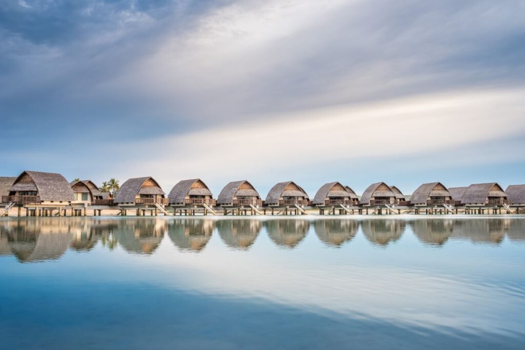 An ocean level view of calm water and a row of over water villas at Fiji Marriott Resort Momi Bay which is one of the best long weekend stays from Brisbane to Fiji - Luxury Escapes