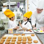 Children with yellow chef hats baking cookies at The Peninsula Bangkok which is home to one of the best kid's clubs in Thailand - Luxury Escapes