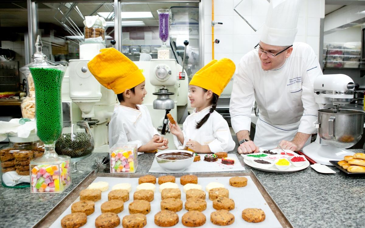 Children with yellow chef hats baking cookies at The Peninsula Bangkok which is home to one of the best kid's clubs in Thailand - Luxury Escapes