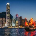 A sail boat on the water at sun down against a backdrop of the sparkling Hong Kong skyline, the perfect place for a cruise stop over - Luxury Escapes