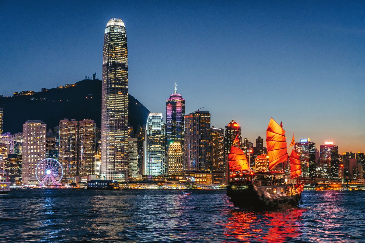 A sail boat on the water at sun down against a backdrop of the sparkling Hong Kong skyline, the perfect place for a cruise stop over - Luxury Escapes
