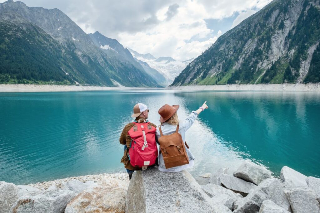A couple point towards rocky mountains overlooking a blue lake in Austria, a destination best explored during the snowy seasons - Luxury Escapes 