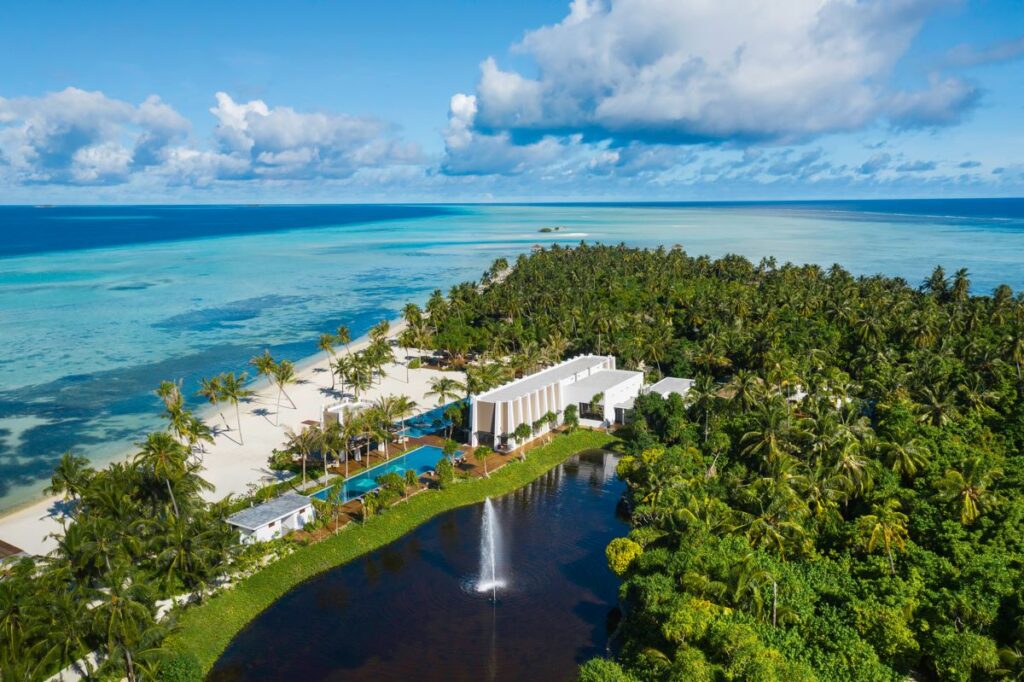 An aerial view of the Pullman Maldives Maamutaa resort and surrounding palm trees and pristine beachfront which is one of the best overwater all-inclusive resorts in the Maldives - Luxury Escapes