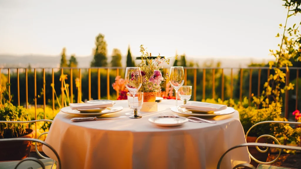 A table at an outdoor restaurant in Tuscany, spread with a white linen table, wine glasses and cutlery - Luxury Escapes