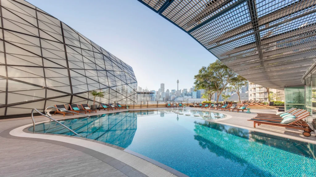 Rooftop pool and deck area at The Grand Star Hotel overlooking the Sydney Tower Eye, which will display a glowing rainbow beacon during the Vivid Sydney 2024 celebrations = Luxury Escapes