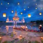 A boat in the river beside a temple with lanterns released for Loy Krathong festival, something you can only experience in Thailand - Luxury Escapes