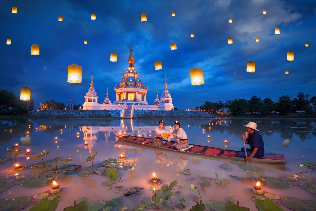 A boat in the river beside a temple with lanterns released for Loy Krathong festival, something you can only experience in Thailand - Luxury Escapes