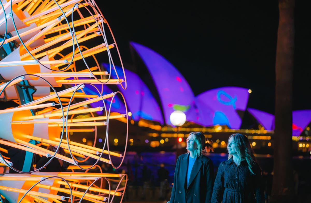Woman enjoying the interactive light display at Vivid Sydney, standing in front of the Opera House - Luxury Escapes 