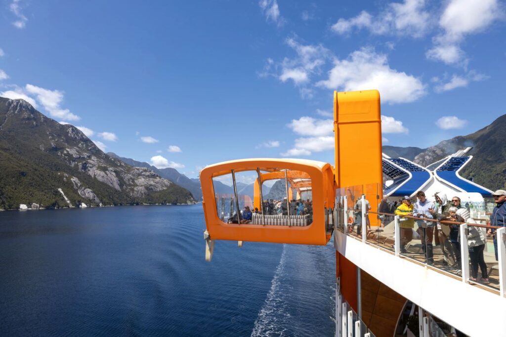 An orange sitting area covered in glass hanging over the edge of the Celebrity Edge, one of the newest Celebrity Cruises ship to sail New Zealand - Luxury Escapes