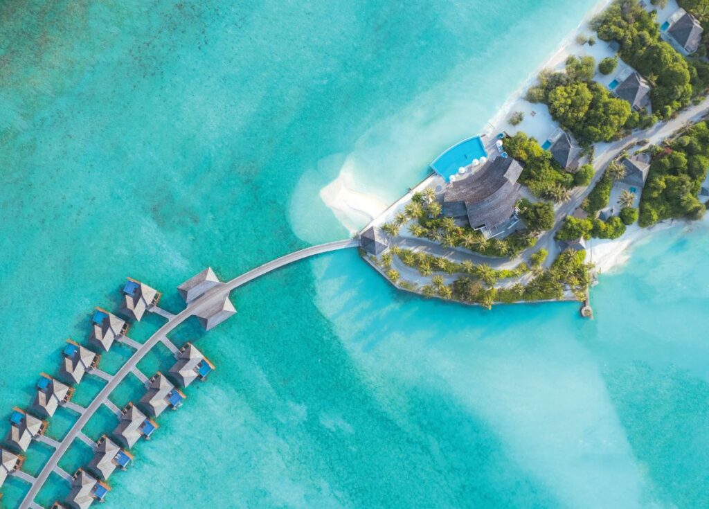 An aerial shot of Hideaway Beach Resort & Spa's floating villas and the blue coastline, one of the best resorts to travel solo in the Maldives - Luxury Escapes