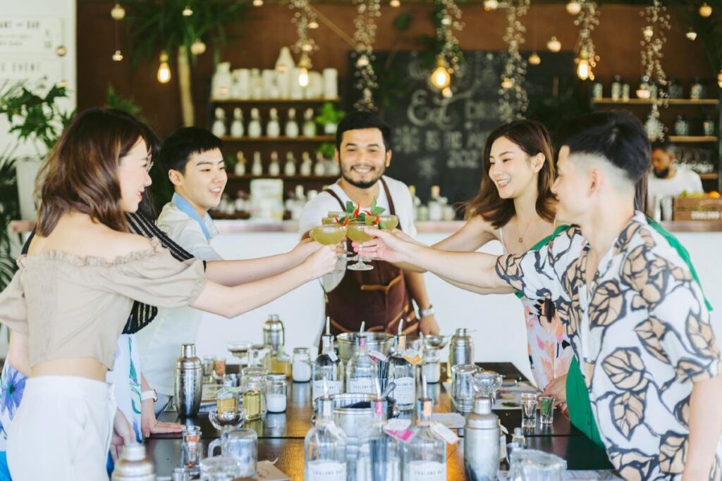 A group of people cheers their cocktails at Chalong Bay Distillery, one of the best places to drink in Phuket - Luxury 
Escapes