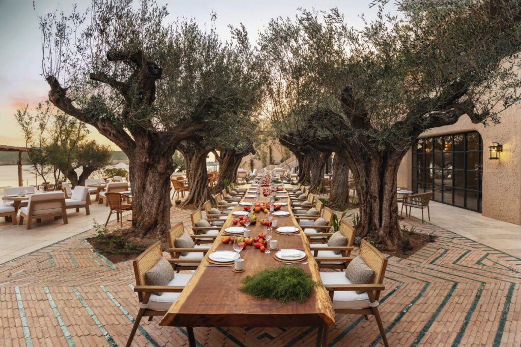 A long dining table set with plates, fruits and other table items framed by tall trees at Six Senses Ibiza, one of the most luxurious resorts in Spain - Luxury Escapes