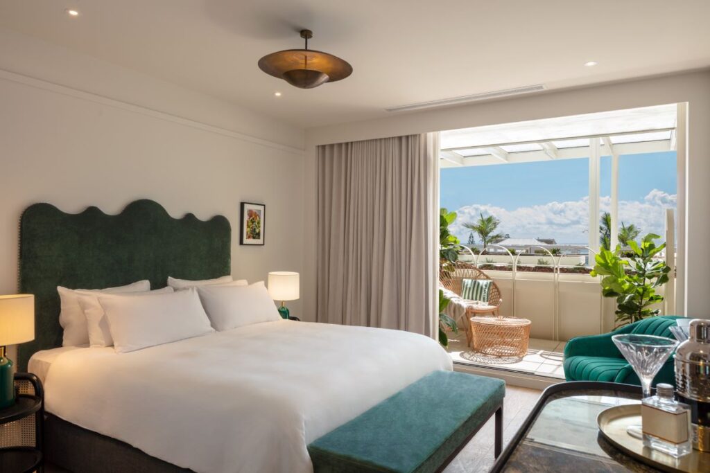 A large bed with a green headboard in a modern room with the door opening out to a sunny balcony, one of many stunning rooms at InterContinental Sorrento Mornington Peninsula - Luxury Escapes