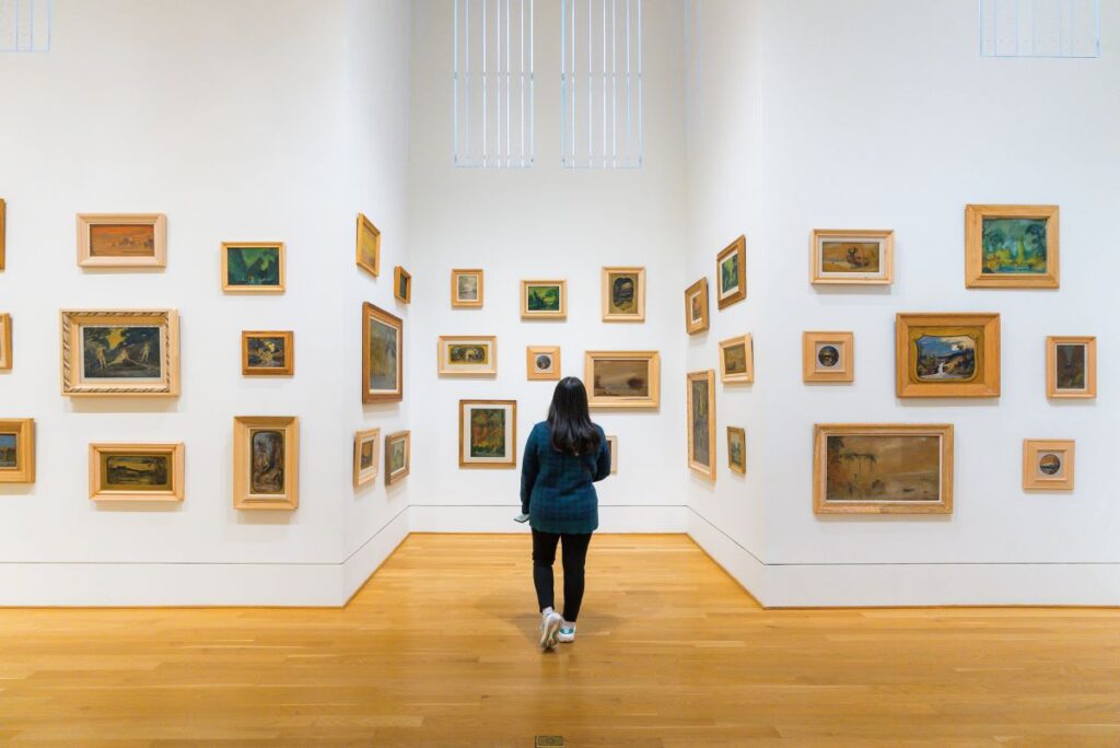 A woman looking at a white wall with a variety of framed artworks in one of Washington DC's art galleries, one of the best things to do while visiting the capital of the USA  - Luxury Escapes