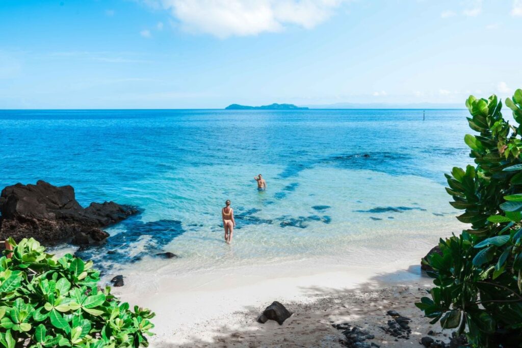 A couple play in the clear blue ocean at Lomani Island Resort, one of the best places to stay when visiting Fiji - Luxury Escapes