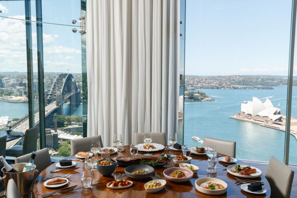 A table overlooking the Sydney Harbour full of plates at Shangri-La Sydney's Altitude restaurant, one of the best places to eat when in Sydney - Luxury Escapes