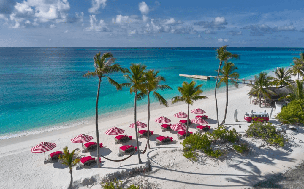 An aerial angle of the Crab Shack's red and white umbrellas dotted along the shoreline at one of the Maldives' most unique resorts; Seaside Finolhu Baa Atoll - Luxury Escapes