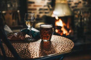 A glass of wine and beer by a fireplace in winter, one of the best things to do in winter in Australia - Luxury Escapes
