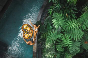 Travel happy couple in love eating floating breakfast in jungle swimming pool. Awakening in morning. Black rattan tray in heart shape, Valentines day or honeymoon surprise, view from above - Dream by Luxury Escapes