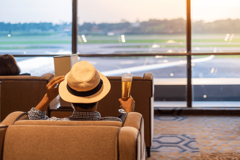 Man with a fedora hat enjoys a beer while at the airport lounge - Luxury Escapes